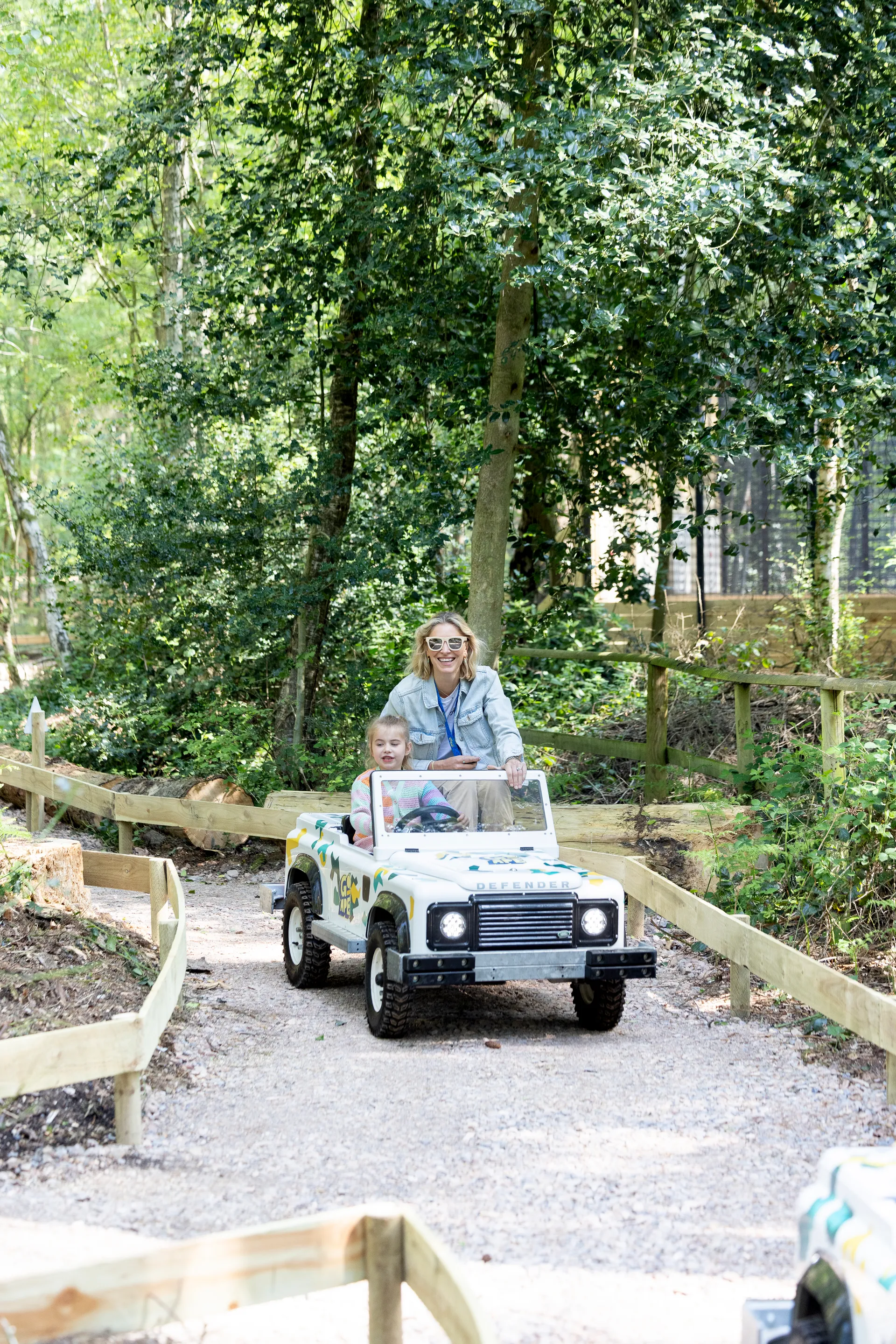 Adult and young person in a Mini Land Rover on a track in the forest.