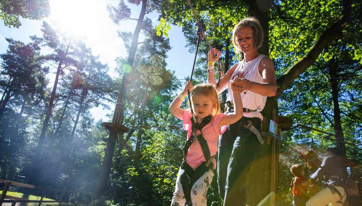 A young girl and her mum hold hands as she negotiates a ropes crossing.