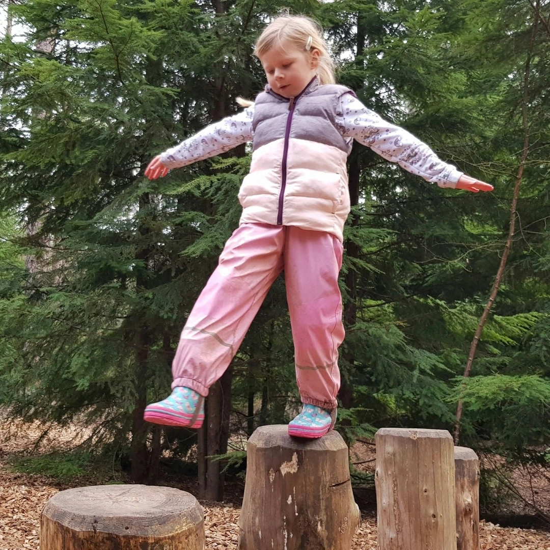 A girl balances on an obstacle in a natural play area